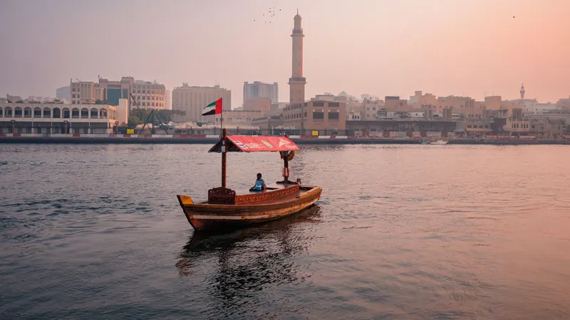 Traditional abra boat on Dubai Creek at sunset with the old waterfront behind it