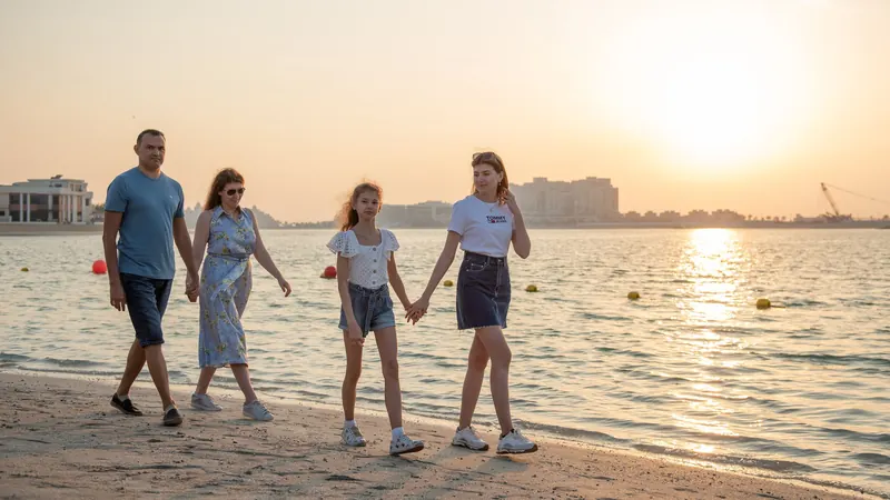 Family of four holding hands while walking on a sandy beach at sunset