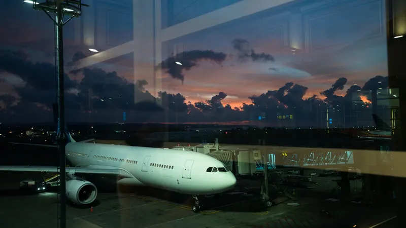 Passenger jet connected to an airport terminal airbridge, seen through glass at dusk