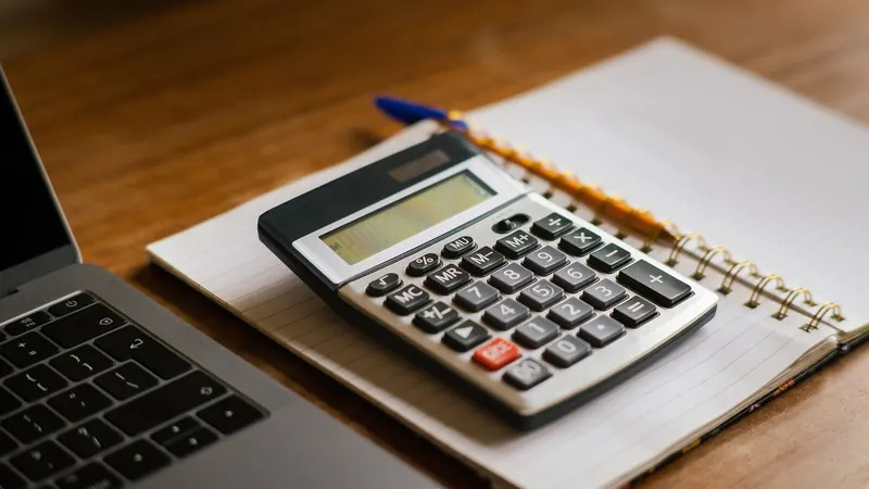 Calculator and notebook on a wooden desk beside a laptop