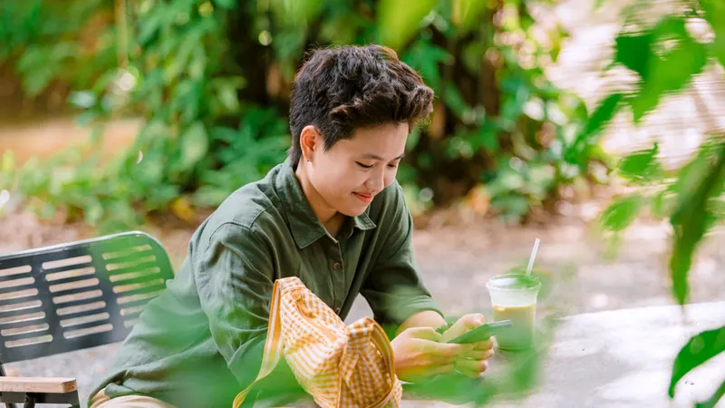 Young person using a smartphone at an outdoor cafe surrounded by greenery