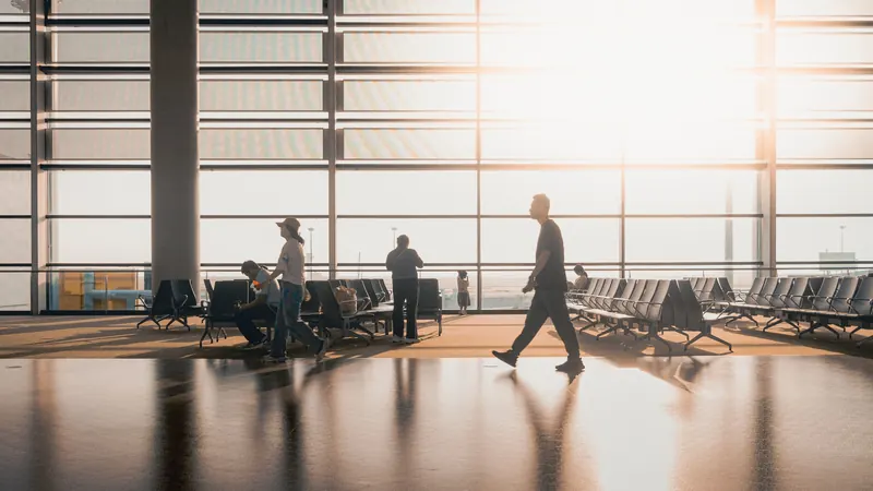 Silhouetted travelers walking through a sunlit airport terminal with rows of seats