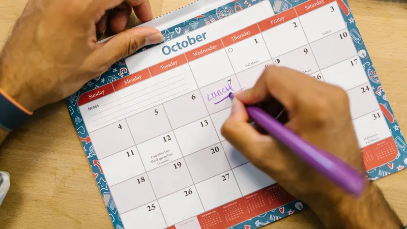 Hand writing a note on a printed monthly calendar with a purple pen