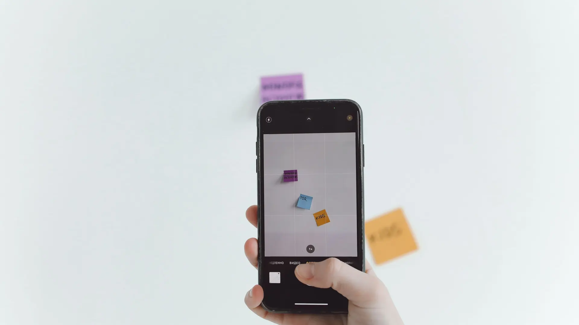 Hand holding a smartphone to photograph paper notes against a plain white wall